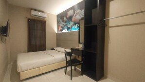 Une petite chambre avec un lit simple, un bureau, une chaise, un miroir et un appareil de climatisation.