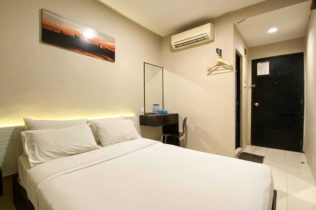 A hotel room with a bed, a nightstand, a mirror, an air conditioning unit, and a door.