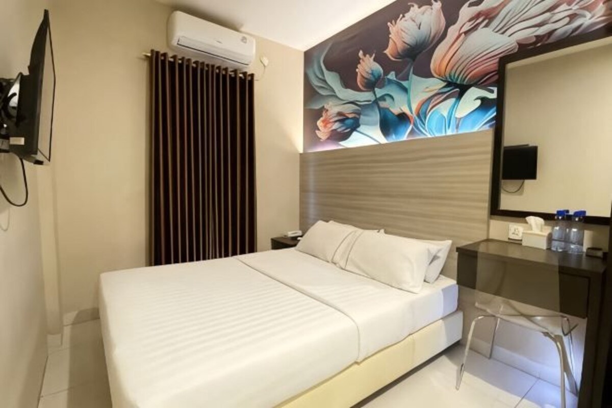 Habitación de hotel con cama, escritorio, silla, televisor y aire acondicionado instalado en la pared.