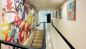 Un couloir avec un escalier, une fresque murale sur le mur de gauche et plusieurs œuvres d’art encadrées sur le mur de droite.
