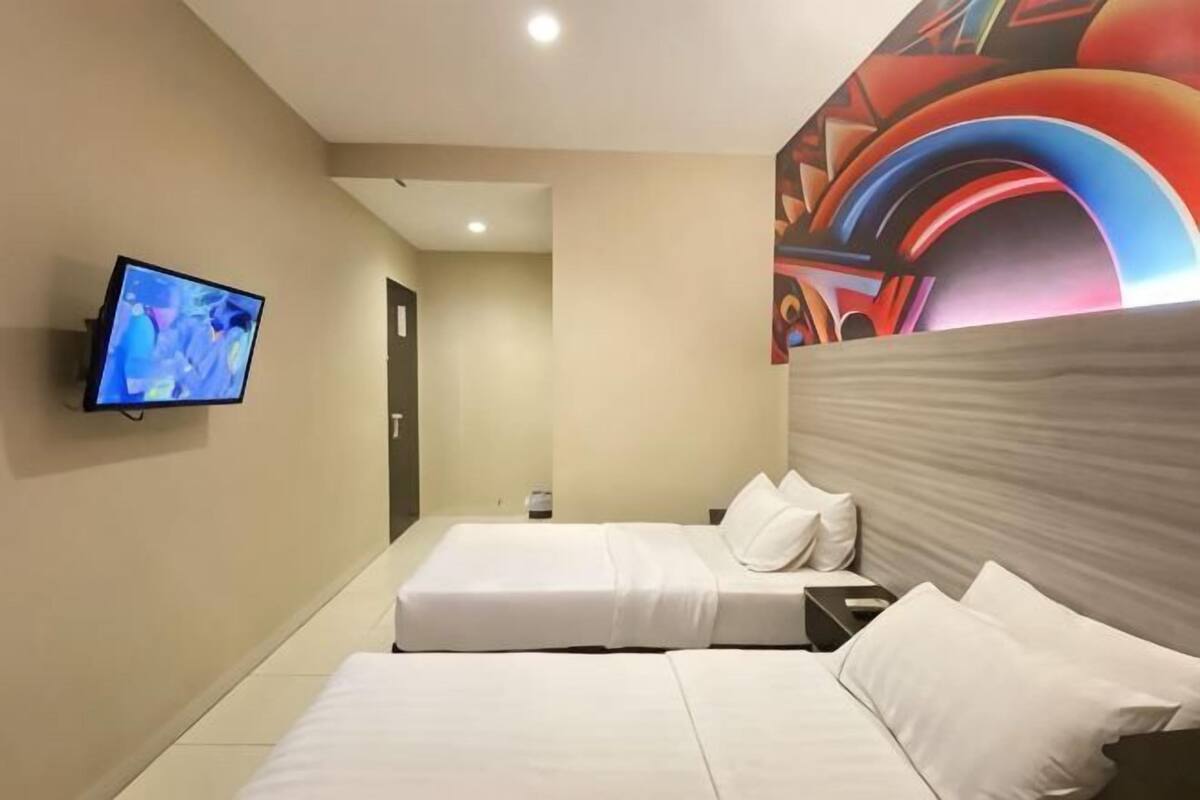 A hotel room with two beds, a television, and a colorful wall mural.