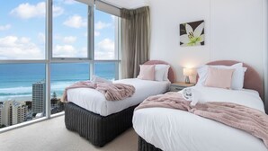 A hotel room with two beds, a large window with a view of the ocean, a wall-mounted flower painting, and a nightstand with a lamp. - Chevron Renaissance - WOWSTAY (Surfers Paradise)