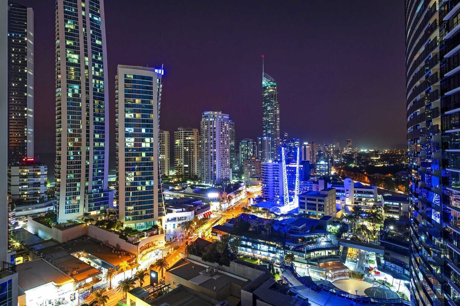 A cityscape at night with high-rise buildings, illuminated streets, and a prominent tower.