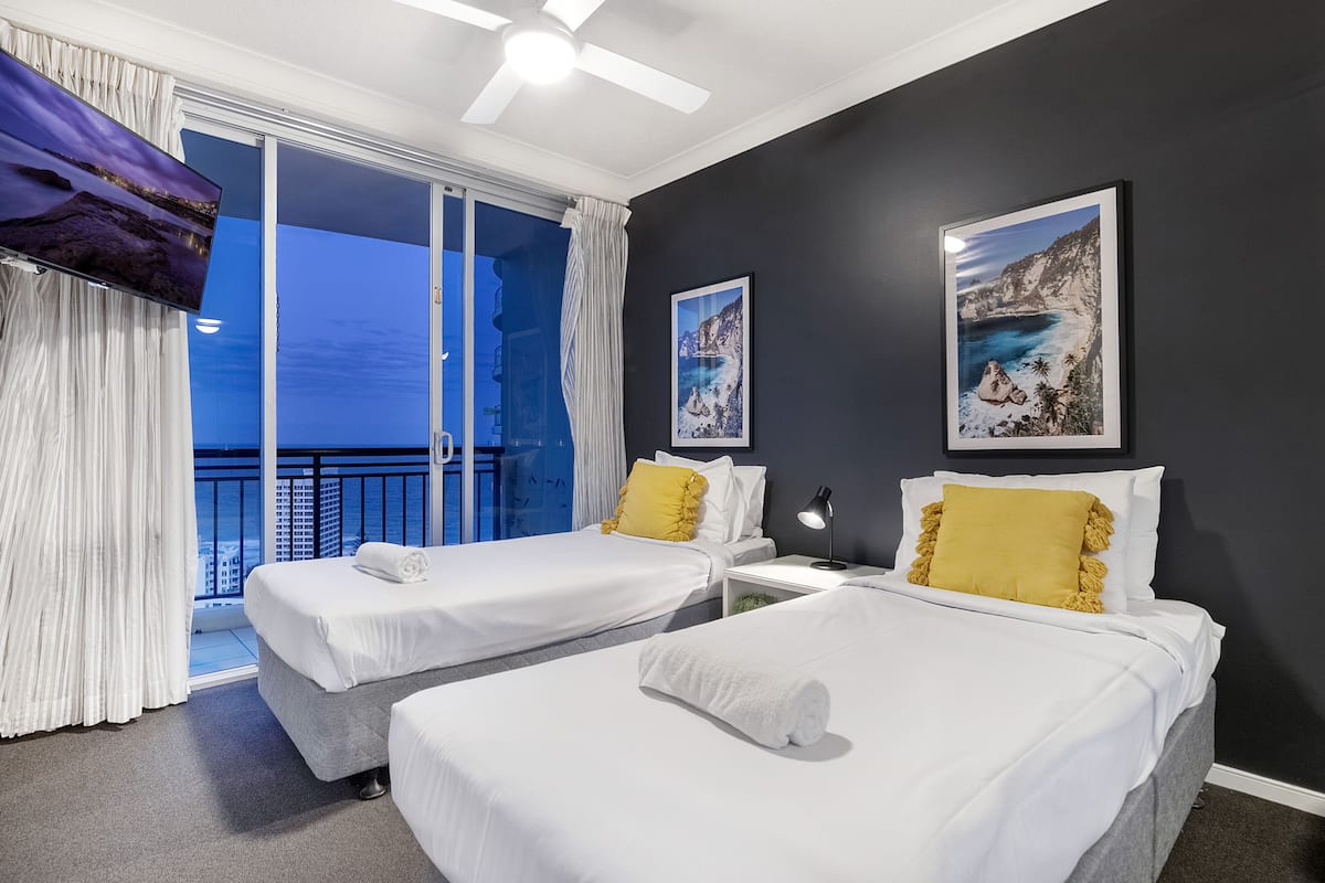Une chambre d’hôtel avec deux lits, un balcon donnant sur la ville et des œuvres d’art accrochées aux murs.