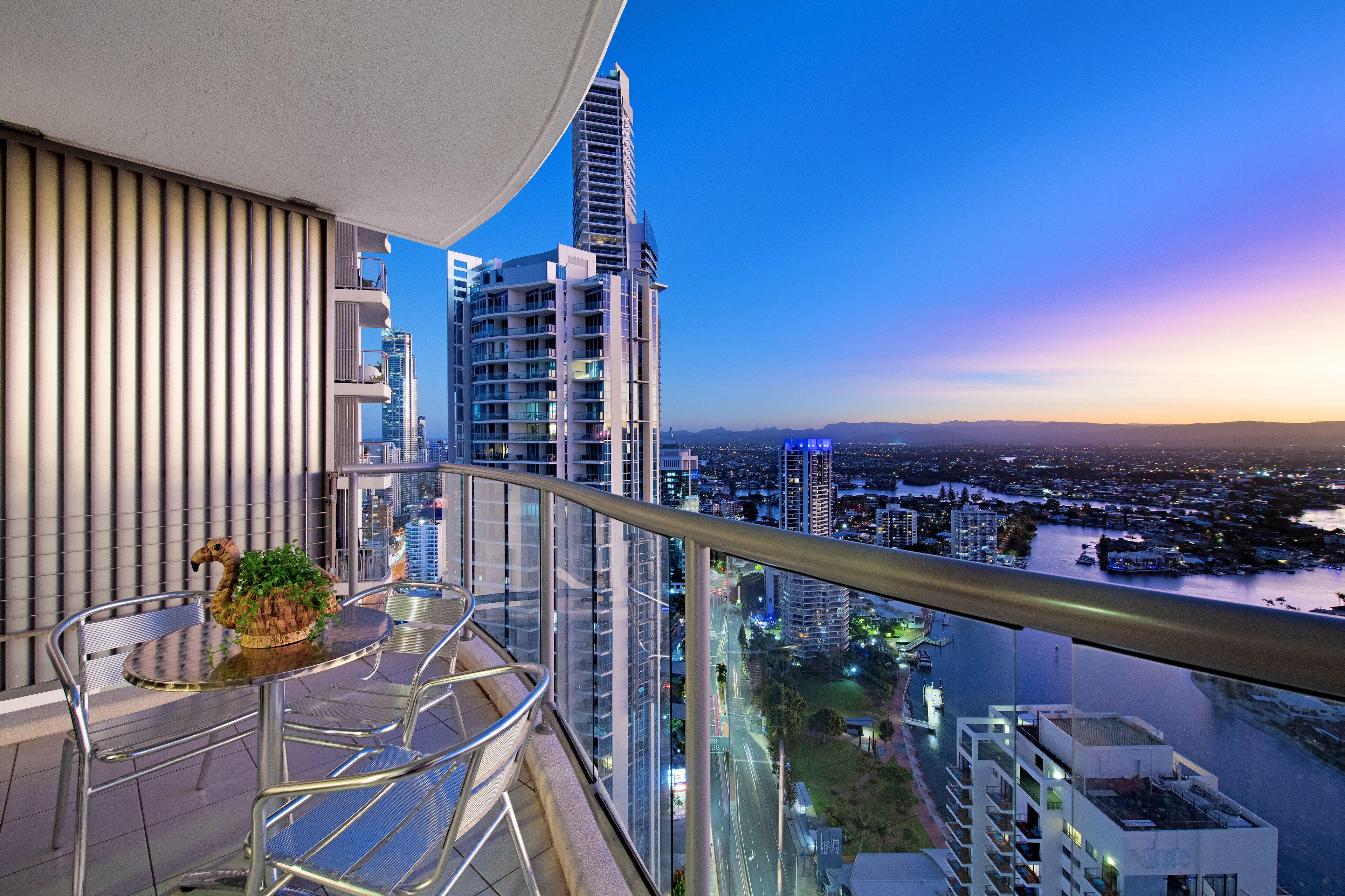A balcony with a view of a cityscape at dusk, featuring modern buildings and a river.
