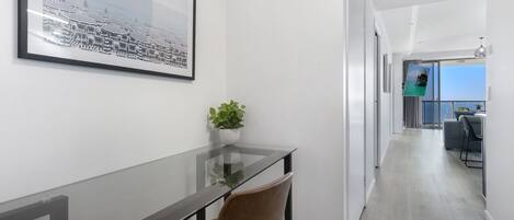 A modern hotel room with a glass table, a brown chair, a framed picture on the wall, and a view of the balcony.