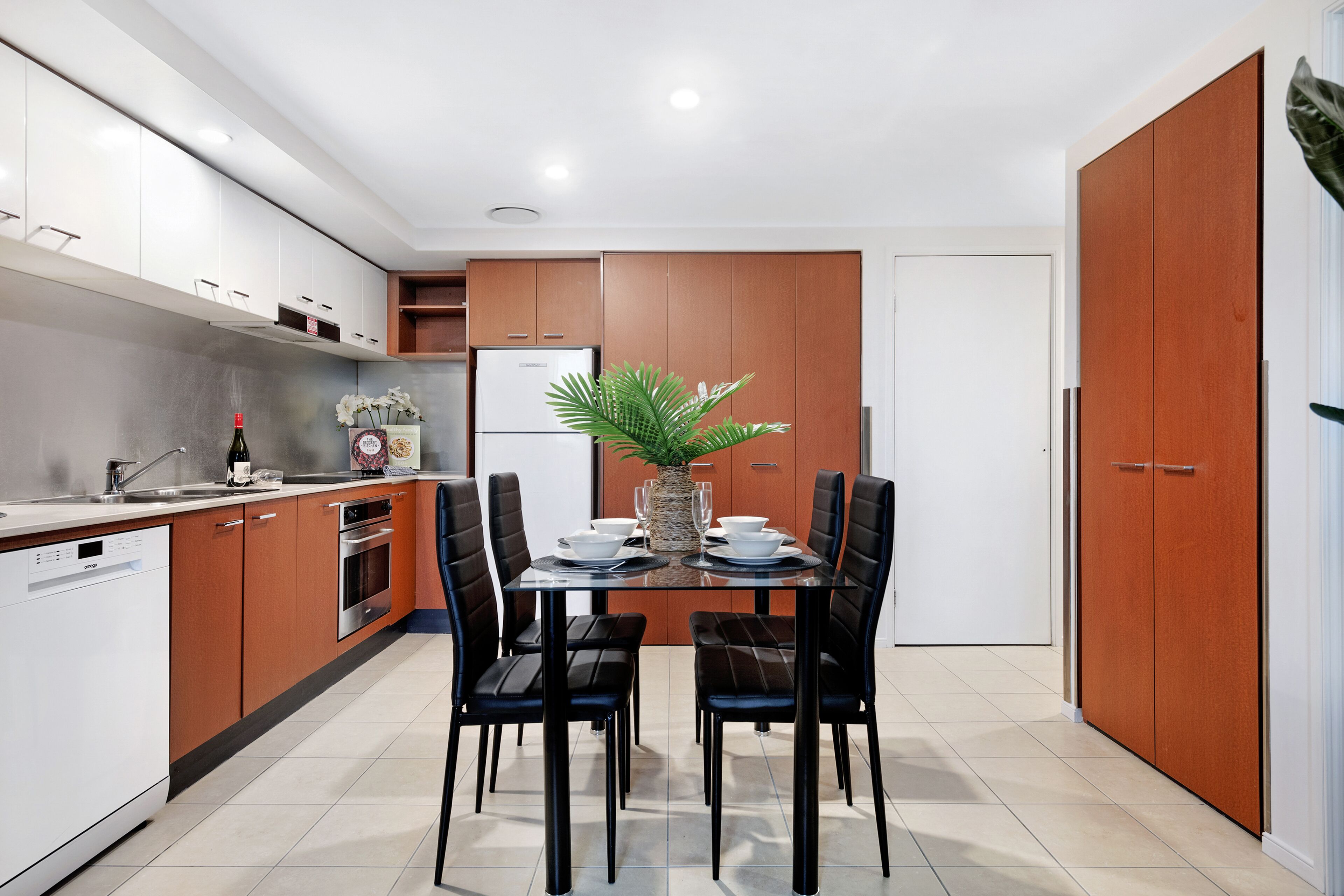 Una cocina moderna con armarios blancos y marrones, una mesa de comedor con sillas negras y una planta en maceta.