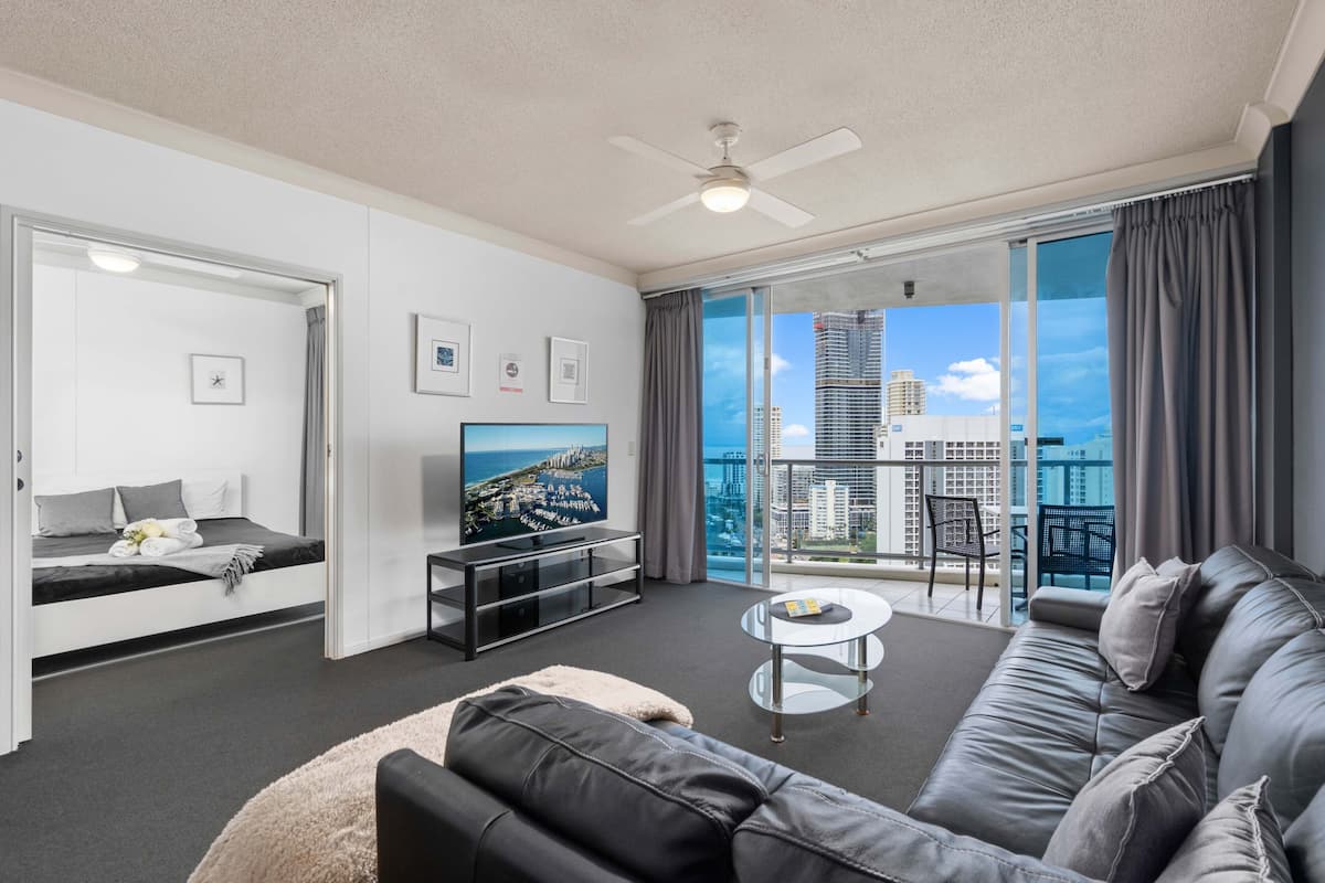 Un salon moderne avec un canapé, un téléviseur, une table basse et un balcon offrant une vue sur la ville.