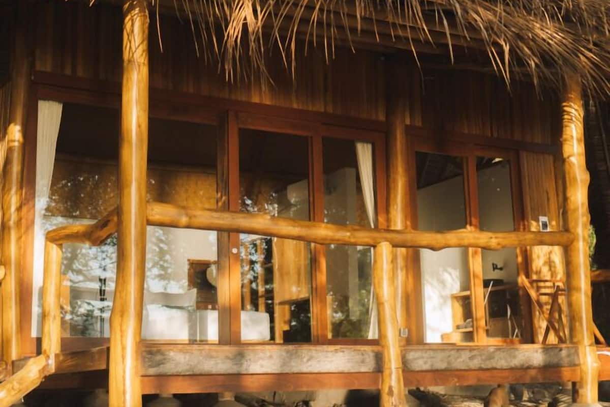 Een houten constructie met rieten dak, grote ramen en een houten leuning.