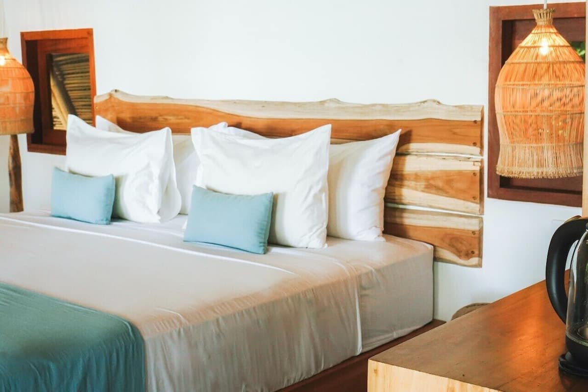 Een bed met een houten hoofdbord, witte en lichtblauwe kussens, en een nachtkastje met een waterkoker.