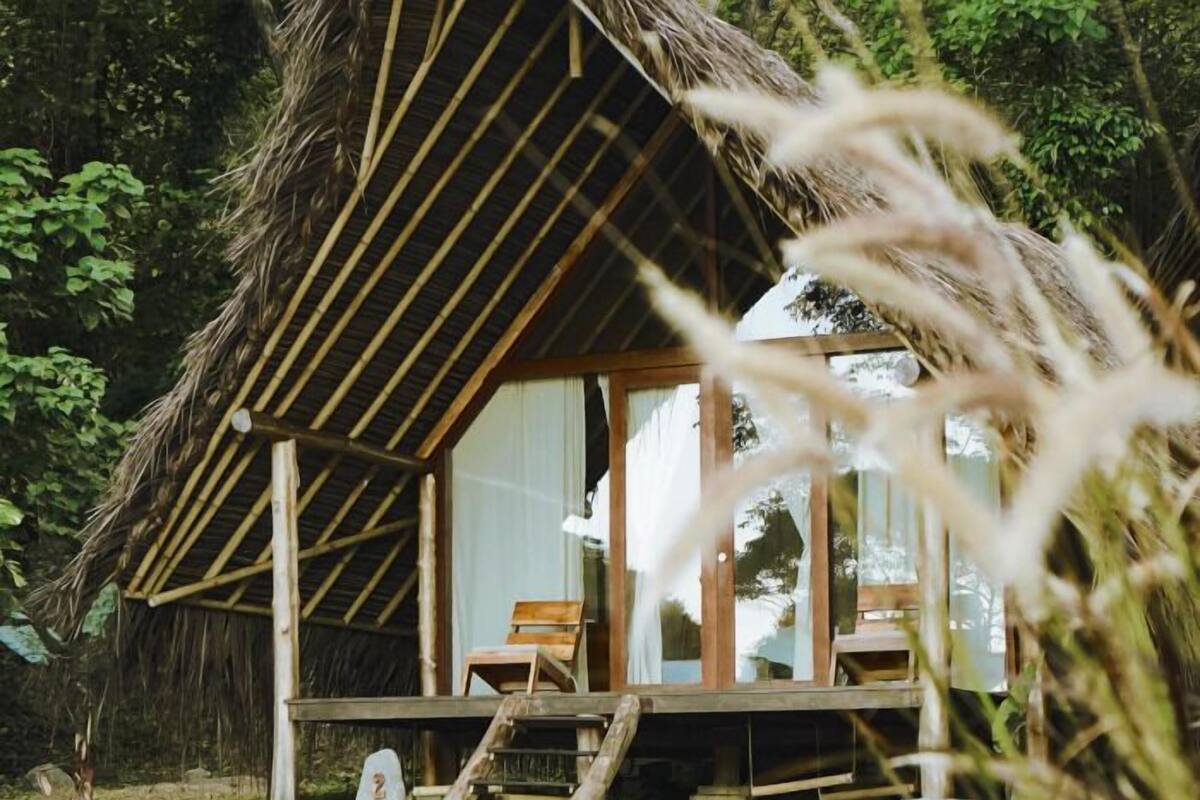 Een rieten hut met een houten veranda, een houten stoel en een trap naar de ingang.