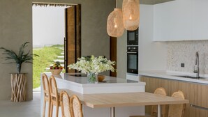 A modern kitchen with a central island, wicker chairs, and a vase of flowers. - Lilly Belle  (Koh Samui)