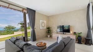 A modern living room with a large gray sofa, a flat-screen TV, and a view of the ocean. - Lilly Belle  (Koh Samui)