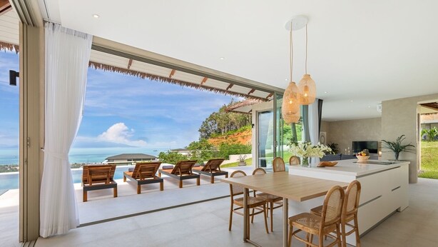 A modern kitchen with a large island, dining area with chairs, and a view of the ocean. - Lilly Belle  (Koh Samui)