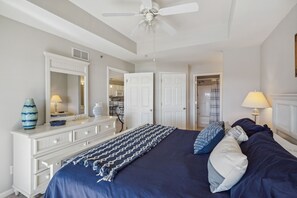Ein Schlafzimmer mit Bett, Kommode, Spiegel, Deckenventilator und einer Tür zu einem Badezimmer.