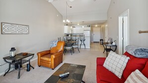 Un salon spacieux avec un canapé rouge, un fauteuil en cuir marron, une table basse et, au fond, un coin repas.