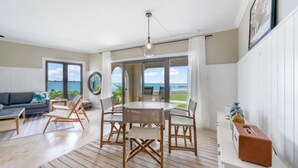 Un salon spacieux avec une table à manger en bois, un canapé et une vue sur l’océan.