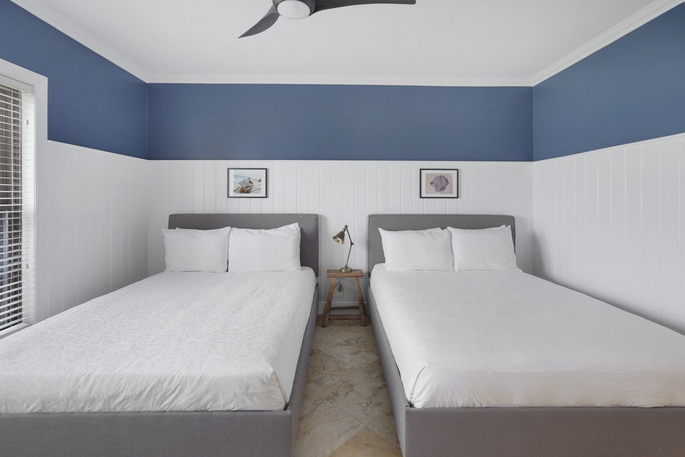 A bedroom with two beds, a ceiling fan, and two framed pictures on the walls.
