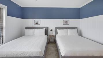 A bedroom with two beds, a ceiling fan, and two framed pictures on the walls.