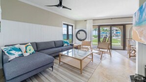 Un salon moderne avec un canapé d’angle gris, une table basse en verre et des fauteuils en osier.