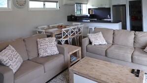 Una sala de estar moderna con un sofá color beige, una mesa de centro de madera y un comedor con sillas blancas.
