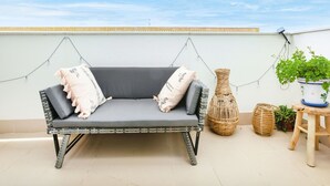 A grey outdoor sofa with cushions, a wicker vase, and potted plants on a tiled patio. - Les Suredes by Interhome (St Antoni de Calonge)