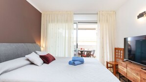 A hotel room with a bed, a TV, a wooden cabinet, and a balcony with a table and chairs. - Les Suredes by Interhome (St Antoni de Calonge)