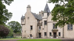 A large, historic building with multiple towers and a well-maintained lawn in front.