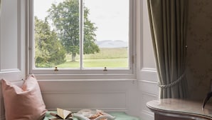 A room with a large window, a green bedspread, a wooden dresser, and a bench.