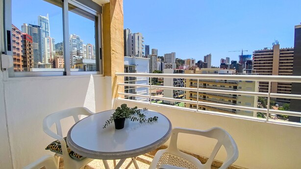 A balcony with a round table and two chairs, overlooking a cityscape with high-rise buildings. - Amsterdam Playa Levante by Interhome (Benidorm)