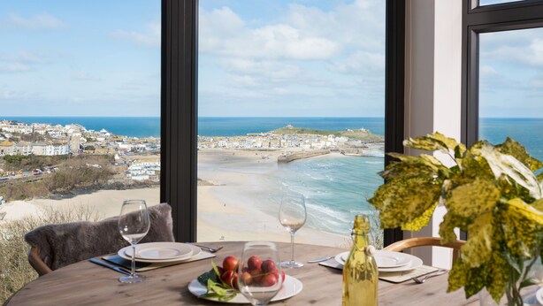 Une table à manger avec des assiettes, des verres et une bouteille, donnant sur une plage et offrant une vue sur l’océan.