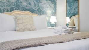 A neatly made bed with a white duvet, a beige knitted throw, and a stack of white towels.