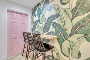 Relax in a tropical oasis with a vibrant wallpaper, pink door, and cozy dining area.