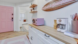 A kitchen with a pink door, white cabinets, a coffee machine, and a wooden shelf with a sign reading "Salt & Sea Inn". - Salt & Sea Inn Unit A-1 Bed 1 Ba Condo w/Pool (Tybee Island)
