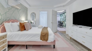 A modern bedroom with a large bed, a television, a white dresser, and a patterned wall. - Salt & Sea Inn Unit A-1 Bed 1 Ba Condo w/Pool (Tybee Island)