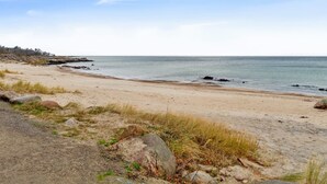 Une plage avec un ciel dégagé, un rivage sablonneux et des rochers.