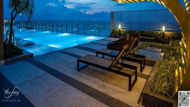 Un espace aménagé au bord de la piscine, avec des chaises longues, un palmier et une vue sur la mer au crépuscule.
