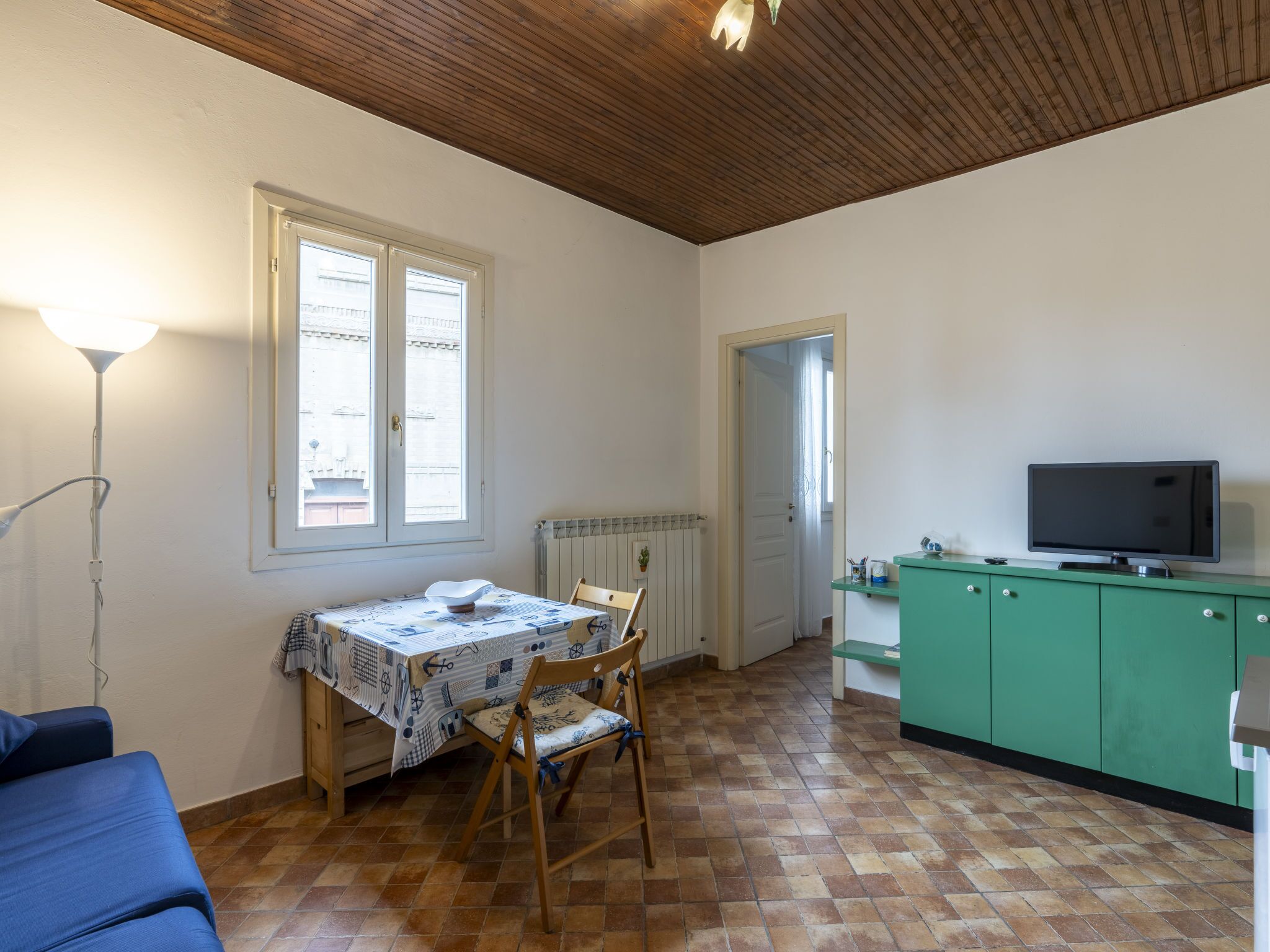 A room with a dining table, chairs, a TV, and a radiator.