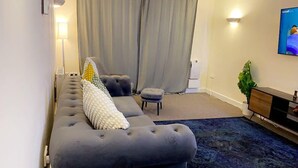 A living room with a grey sofa, a small ottoman, a blue rug, a television, and a plant. - Stunning 2-Bed Apartment in London (London)