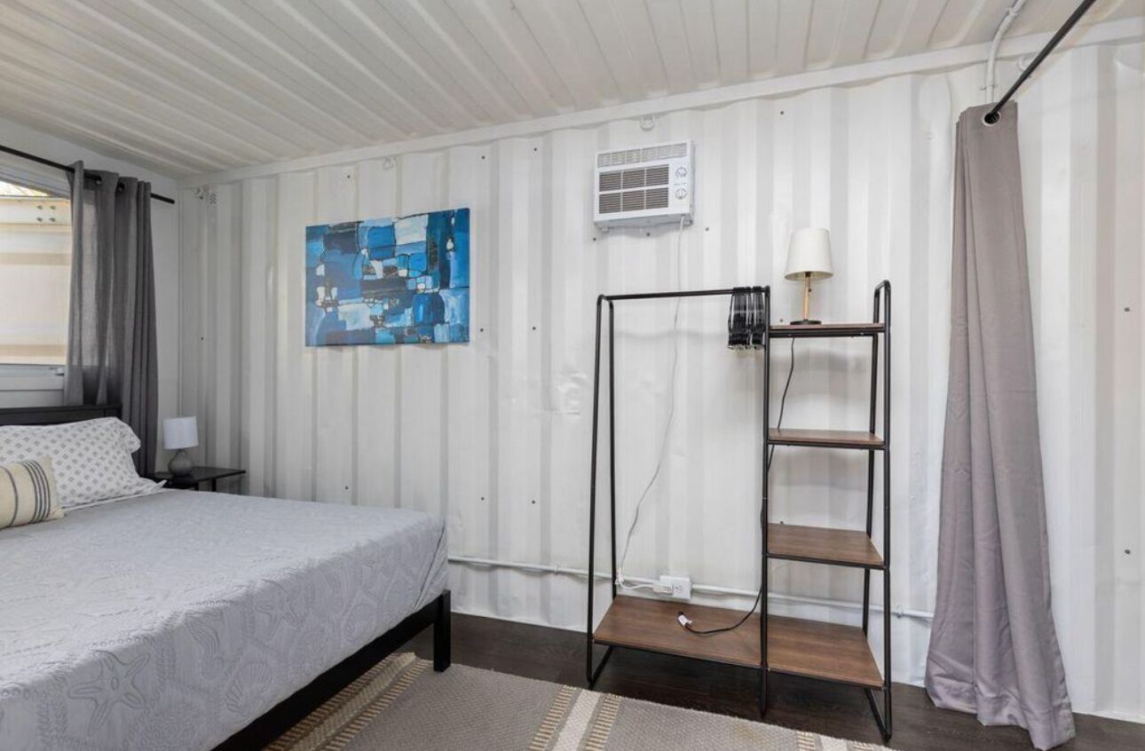 Camera da letto con un letto, condizionatore d'aria a parete, un quadro, una mensola in metallo e una tenda.