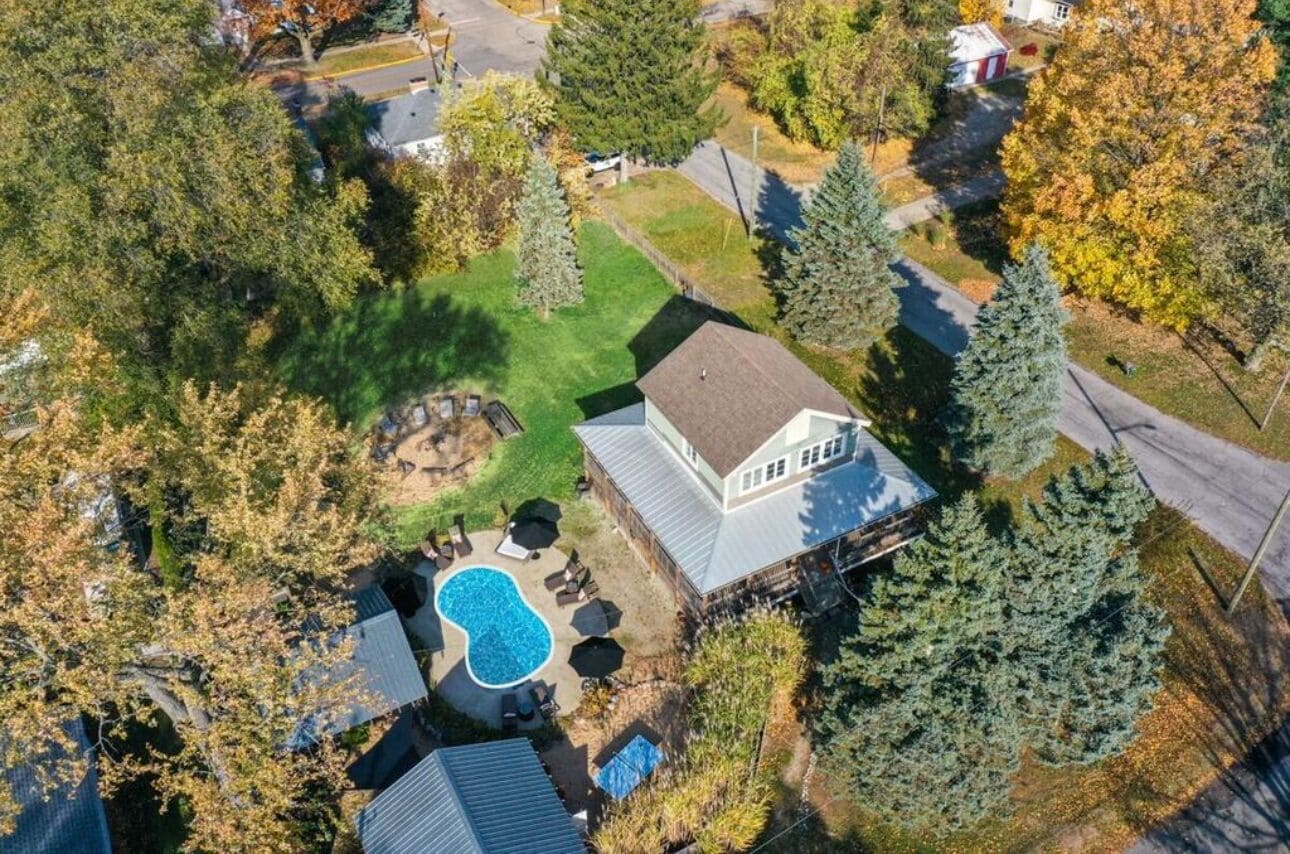 An aerial view of a residential property with a swimming pool, a fenced yard, and a house with a sloped roof.