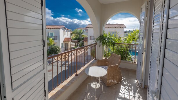 Ein Balkon mit weißem Tisch und Korbstühlen, mit Blick auf eine Straße und Gebäude.