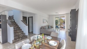 Ein Essbereich mit einem Holztisch, gedeckt für sechs Personen, einer Treppe, einer Couch und Blick ins Freie.