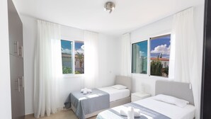Ein Hotelzimmer mit zwei Betten, einem Fenster mit Blick auf Palmen und einer weißen Deckenleuchte.