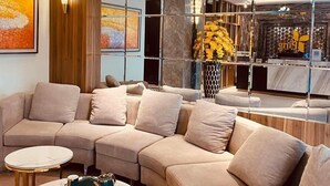 Un soggiorno moderno con un divano componibile, due tavolini, un lampadario e uno specchio che riflette una vetrina di abbigliamento.