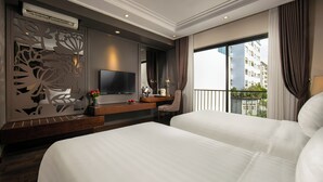 Camera d'albergo con due letti, una TV, una scrivania con sedia e un'ampia finestra che dà su degli edifici.