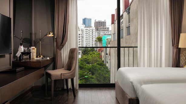 Camera d'albergo con un letto, una scrivania con una lampada, una sedia e vista sulla città dal balcone.