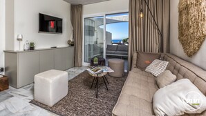 A modern living room with a sofa, ottoman, and a small table with magazines. There is a TV mounted on the wall and a large window with curtains. - Nico | Sea Siew - Pool - Beach (Sitio de Calahonda)
