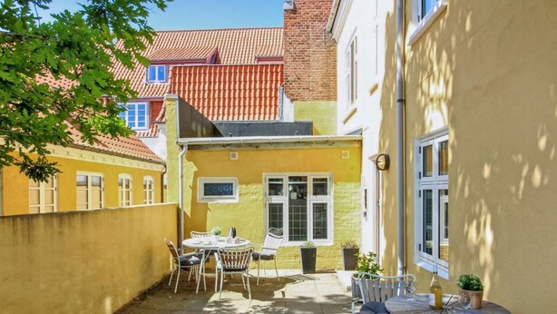 Un patio con una pared amarilla, una mesa y sillas, y una ventana.