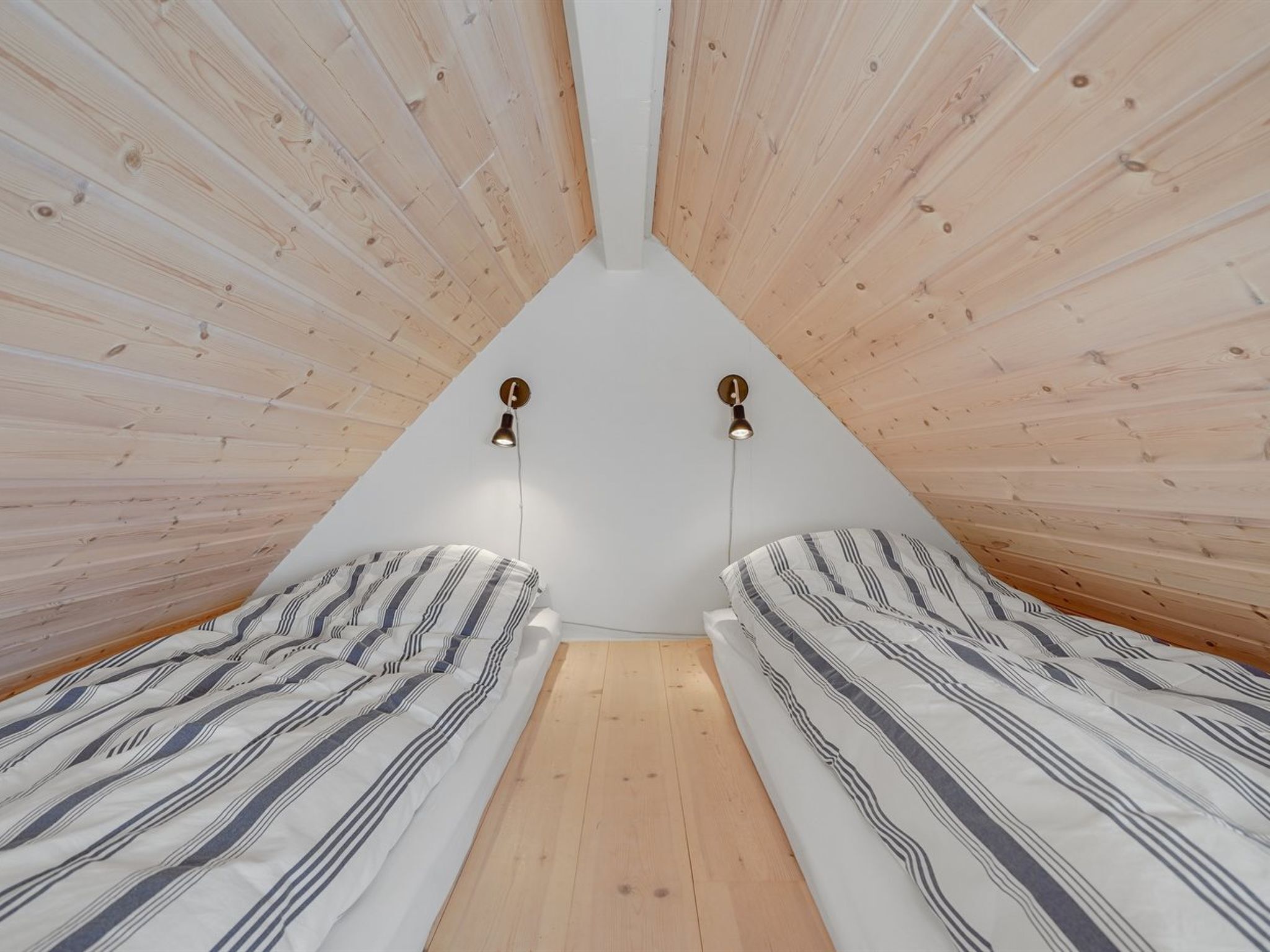 Una stanza con due letti, soffitto in listelli di legno e due lampade a parete.